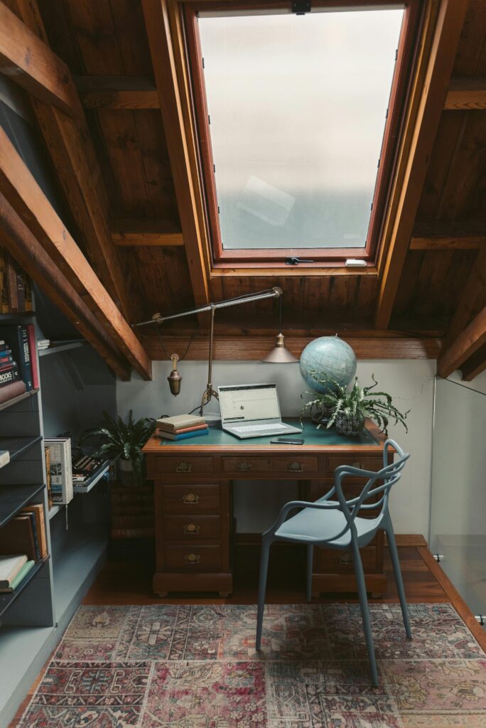 A cozy attic office space with a vintage desk, globe, and books under a skylight.